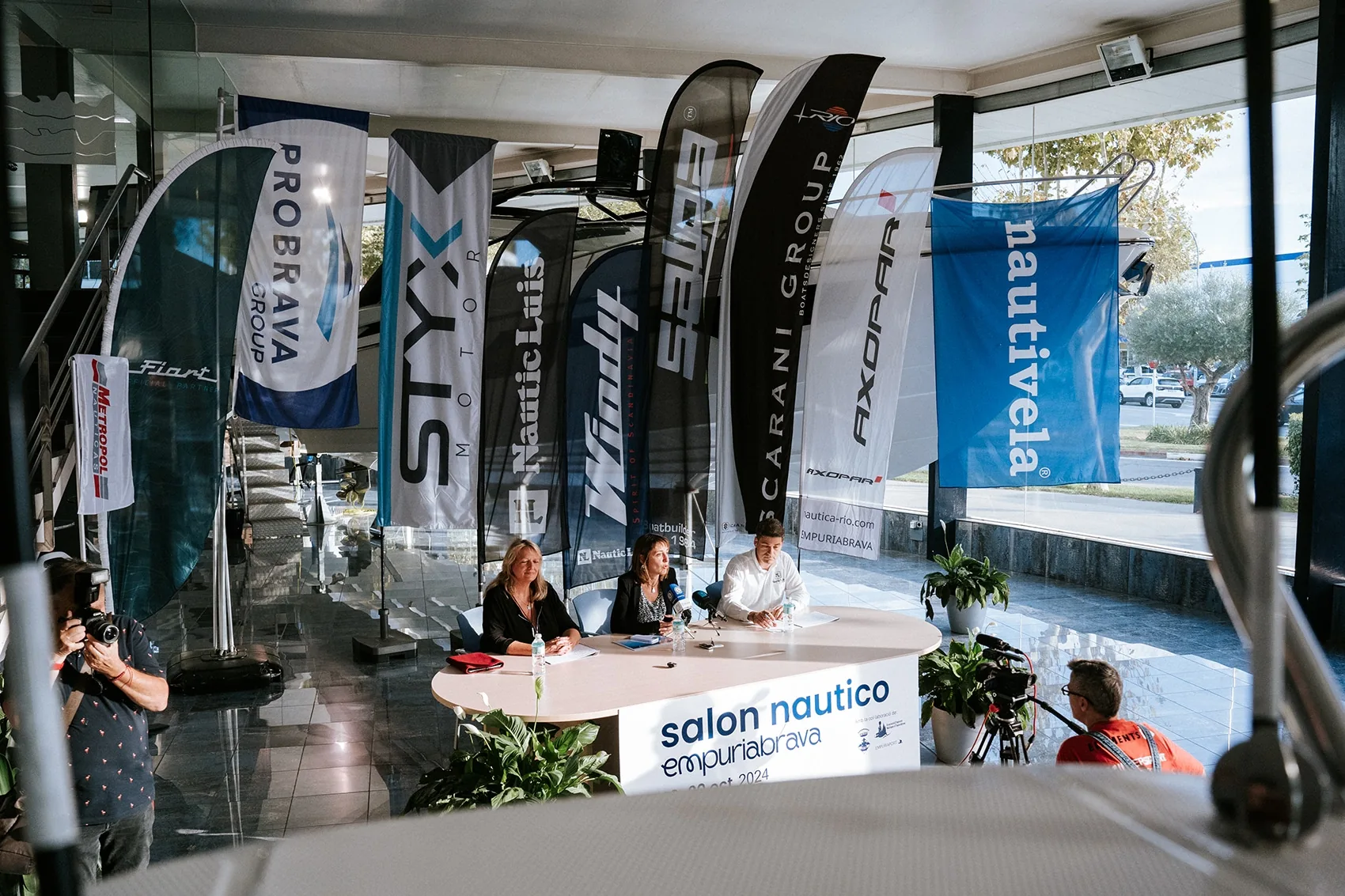 Empuriabrava Boat Show booth with counter, three people and nautical flags.