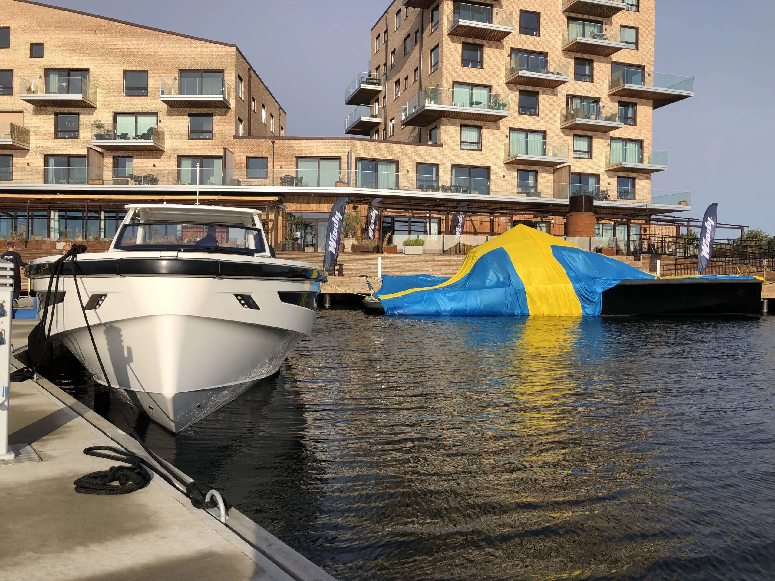 Windy SR 60 viewed from the bow, moored alongside a dock, with buildings and another covered boat in the background