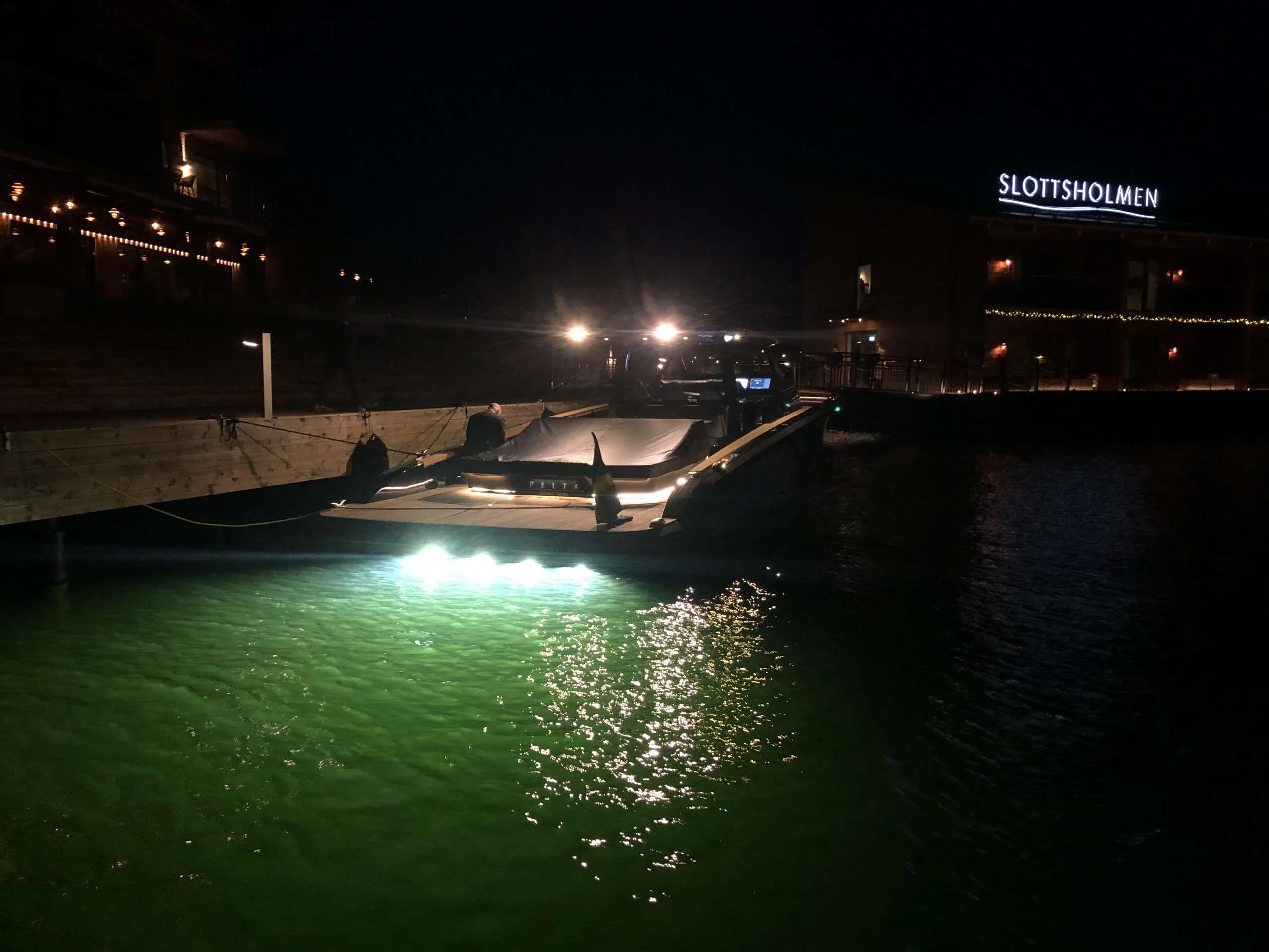 Exterior of the Windy SR 60 moored at night, viewed from the stern, with green underwater lights.