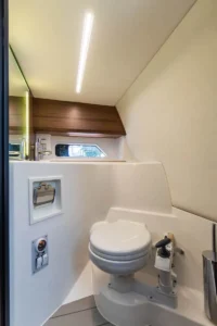 Intérieur de la salle de bain du Windy 27 Solano RS, vu de face, avec toilettes marines, fenêtre latérale et meuble en bois.