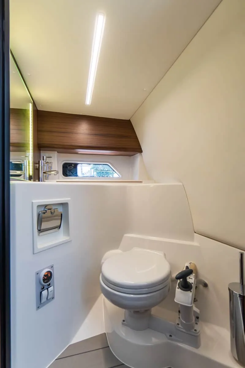 W27SOLANO (17) Intérieur de la salle de bain du Windy 27 Solano RS, vu de face, avec toilettes marines, fenêtre latérale et meuble en bois.