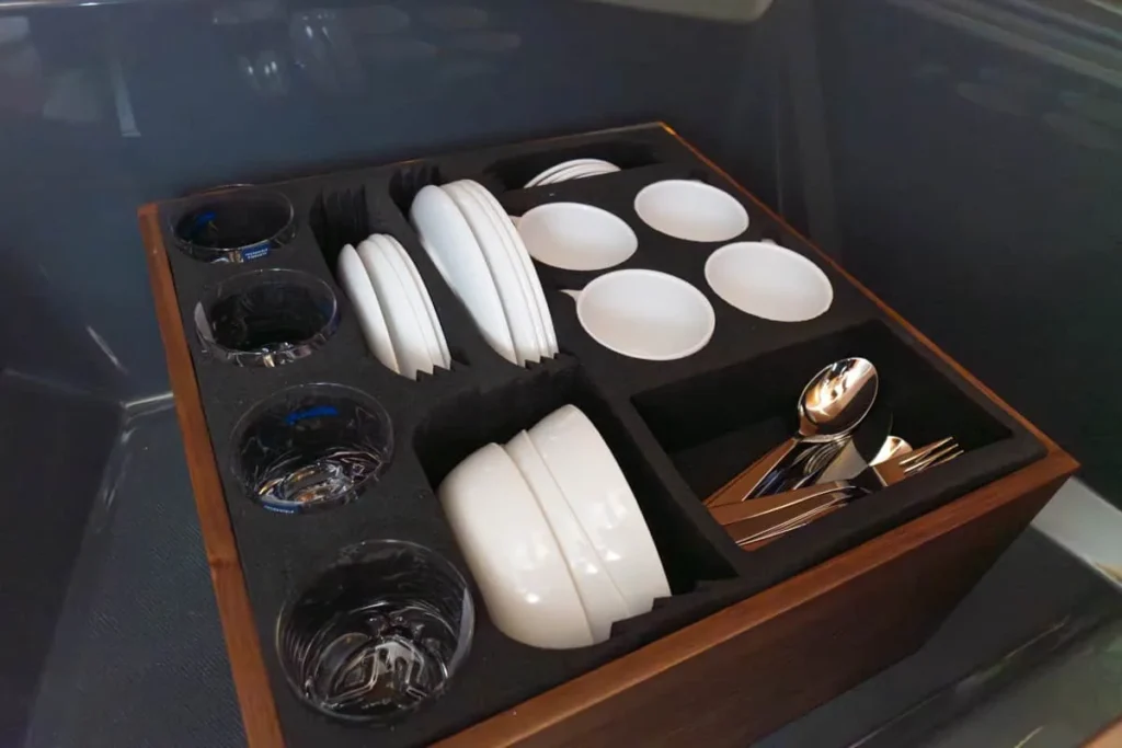 Intérieur du Windy 27 Solano RS avec un plateau de vaisselle, des verres, des assiettes, des couverts et des verres à pied.