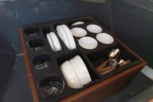 Intérieur du Windy 27 Solano RS avec un plateau de vaisselle, des verres, des assiettes, des couverts et des verres à pied.