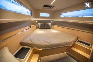 Interior de Windy SR44 Blackhawk, vista de proa con cama doble, almohadas, ventanas laterales y escalones.