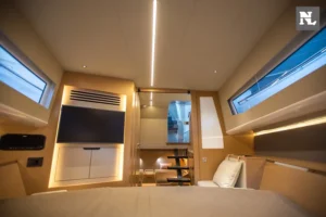 Interior del Windy SR44 Blackhawk 27, visto desde la cama, con televisor, escalera, ventanales y mobiliario.