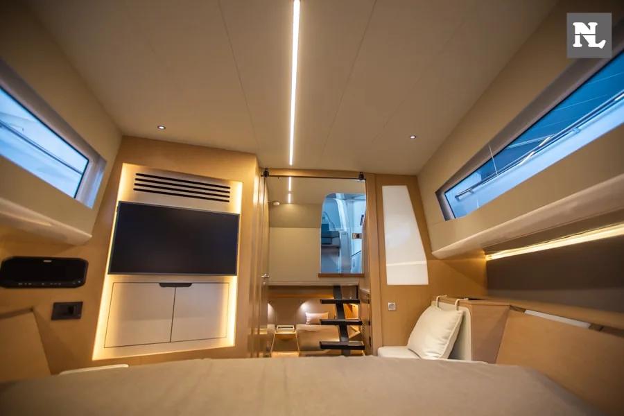 Interior del Windy SR44 Blackhawk 27, visto desde la cama, con televisor, escalera, ventanales y mobiliario.