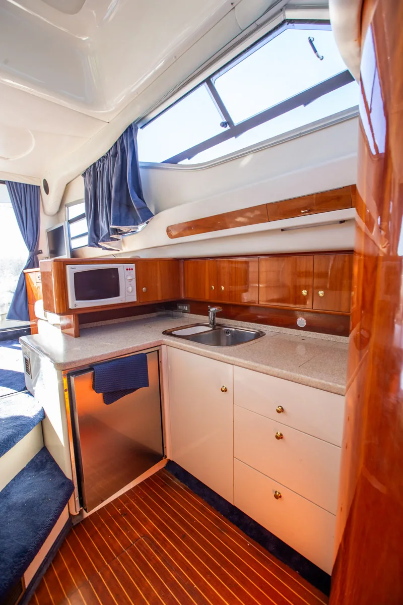 Cranchi Atlantique 40 – Cocina galley Pantryküche der gebrauchten Cranchi Atlantique 40 in Empuriabrava – Nautic Luis, mit L-förmiger Arbeitsplatte, Mikrowelle und Holzmöbeln