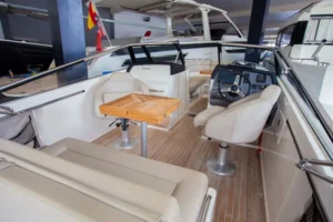 Interior de la Draco 27 R Sport, visto desde popa, con asientos, mesa de madera, timón y consola de mando.