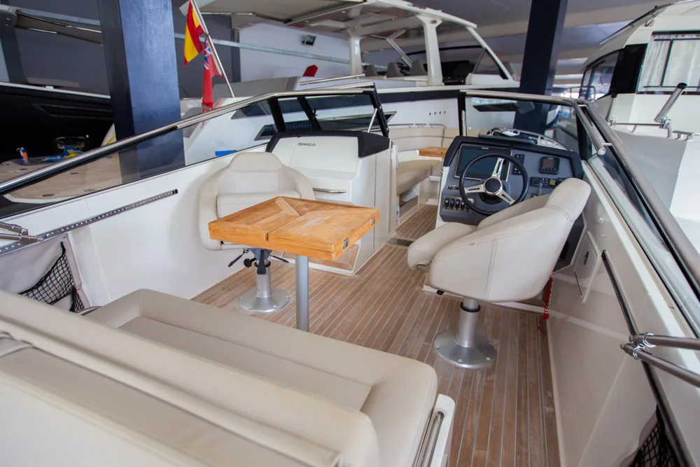 Interior de la Draco 27 R Sport, visto desde popa, con asientos, mesa de madera, timón y consola de mando.