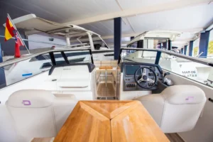 Draco 27 Rsport, interior visto desde popa, mesa de madera cerrada, puesto de mando y asientos visibles.