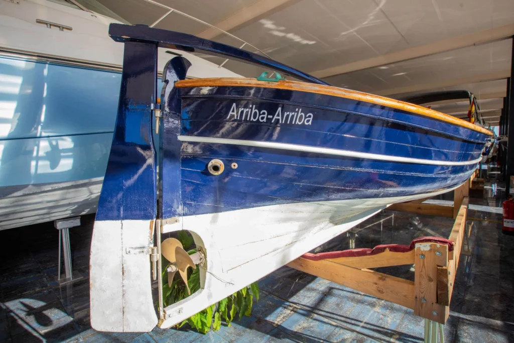 LLAUT 32P von achtern im Innenbereich gesehen, mit blauem Rumpf, sichtbarem Propeller und dem Namen „Arriba-Arriba“.