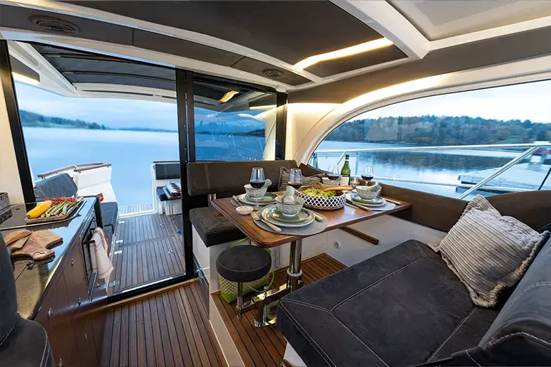 Interior del Marex 330 Scandinavia con salón, mesa de comedor, cocina y vistas al agua desde el camarote.