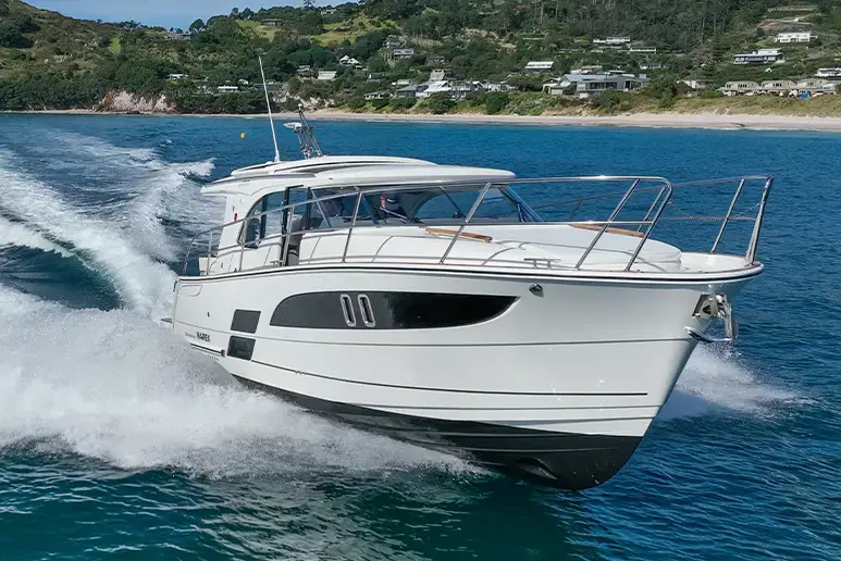 Marex 330 Scandinavia navegando de perfil, con cabina cerrada, proa abierta y estela sobre el mar junto a la costa.