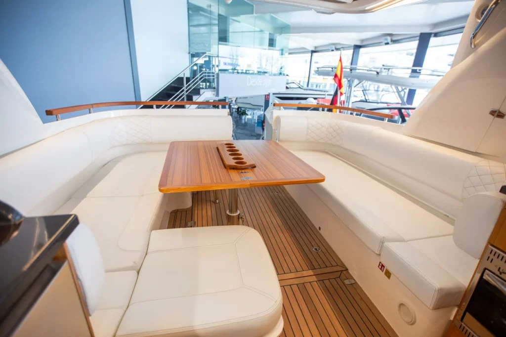 Intérieur du Marex 360 Cabriolet Cruiser, salon vu depuis la poupe avec un canapé en U, une table en bois et un plancher en teck.