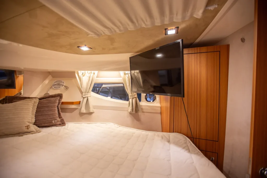 Intérieur du Marex 360 Cabriolet Cruiser : cabine avec lit, télévision, fenêtre avec rideaux et armoire en bois.