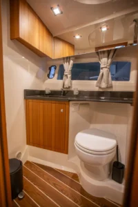 Intérieur du Marex 360 Cabriolet Cruiser : salle de bain avec lavabo, toilettes, placards en bois et fenêtre avec rideaux.