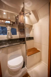 Intérieur du Marex 360 Cabriolet Cruiser : salle de bains avec toilettes, lavabo, douche, fenêtre et sol en teck.