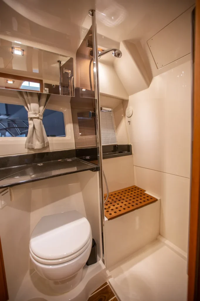 Intérieur du Marex 360 Cabriolet Cruiser : salle de bains avec toilettes, lavabo, douche, fenêtre et sol en teck.