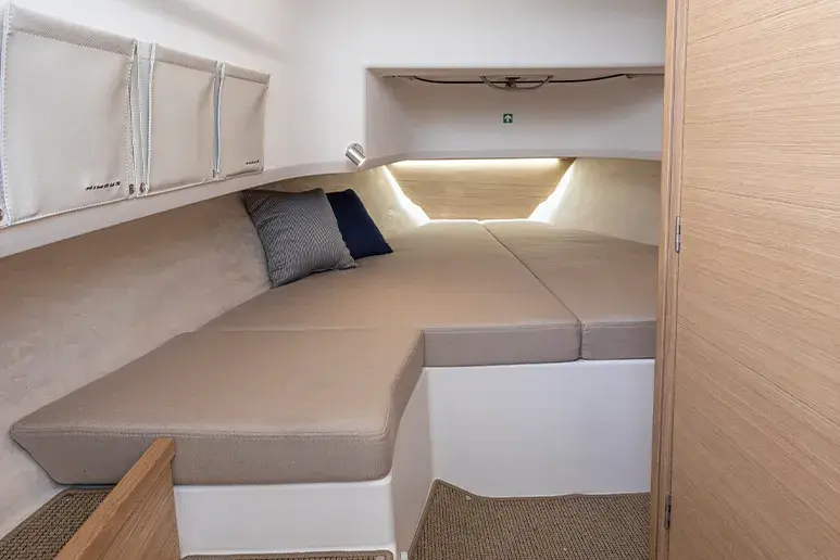 Interior de Nimbus C9 con cabina, literas tapizadas, almohadas, armarios y ventana frontal.