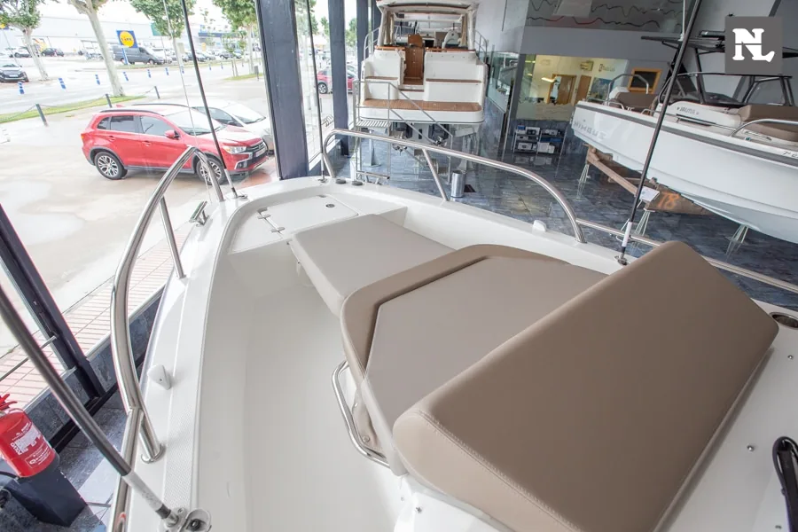 Nimbus T8: cubierta de proa vista desde el interior, con solárium acolchado, pasamanos y embarcaciones en exposición.