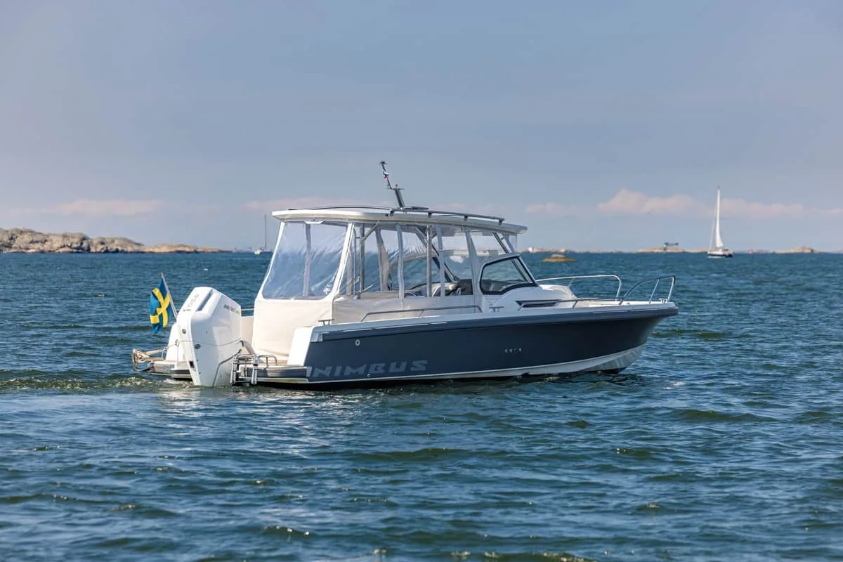 T9-GALERIE-13 Außenansicht der Nimbus T9 im Profil, mit geschlossener Kabine, Außenbordmotor und Segelboot im Hintergrund.