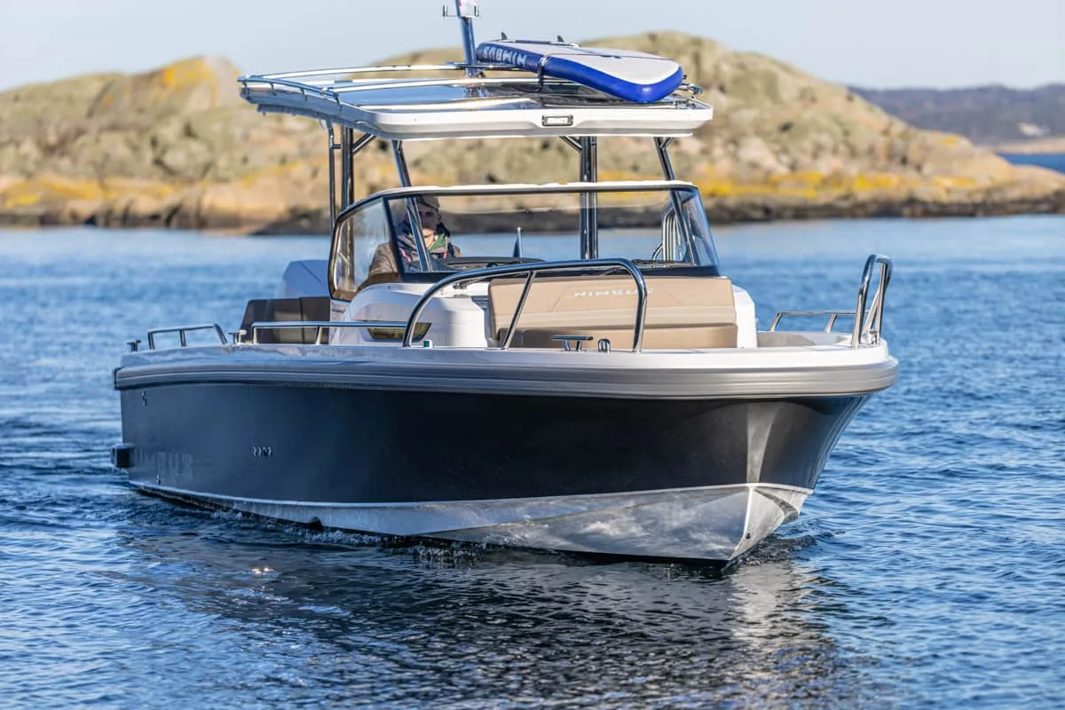 T9-GALERIE-4 Nimbus T9 von vorne auf dem Wasser gesehen, mit Hardtop, Windschutzscheibe, Mittelkonsole und felsigen Küsten im Hintergrund
