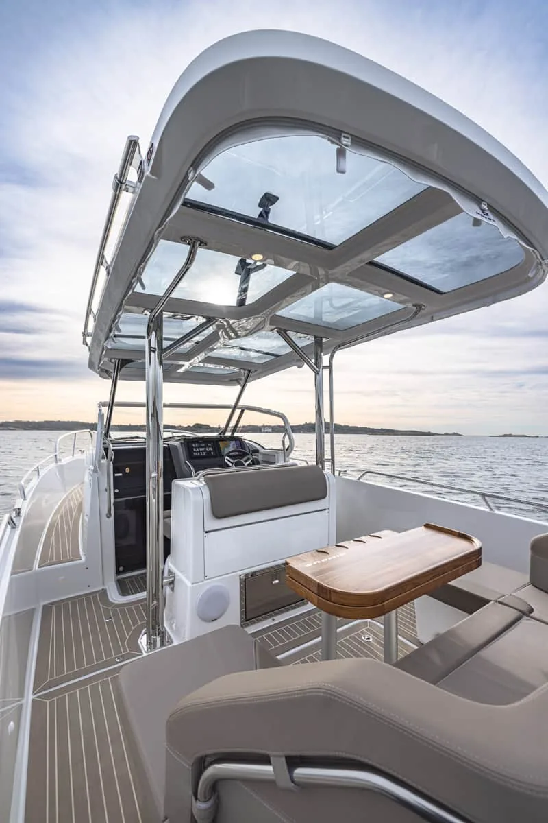 T9-GALERIE-8 Nimbus T9 im Außencockpit, mit einem verglasten Hardtop, Steuerstand, Sitzen und einem Holztisch auf dem Wasser.