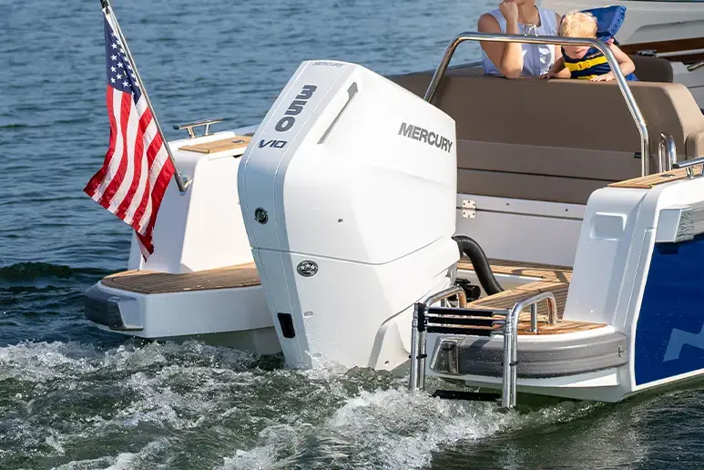 Exterior trasero del Nimbus W9 en el agua, con motor fueraborda Mercury y bandera estadounidense visible