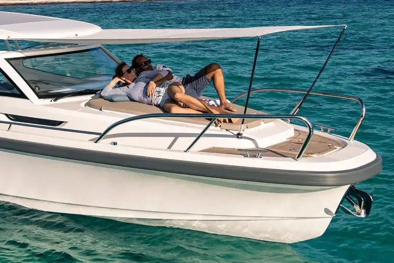Exterior del Nimbus W9 visto de lado, con dos personas tumbadas en la proa y toldo extendido sobre el mar.