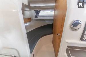 Innenraum im Bug der Parker 800 Pilothouse, mit einem Bett, einem Fenster mit Vorhang und einer Holztür.