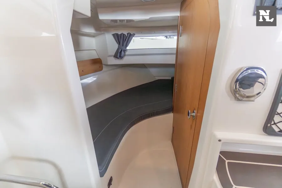 Innenraum im Bug der Parker 800 Pilothouse, mit einem Bett, einem Fenster mit Vorhang und einer Holztür.
