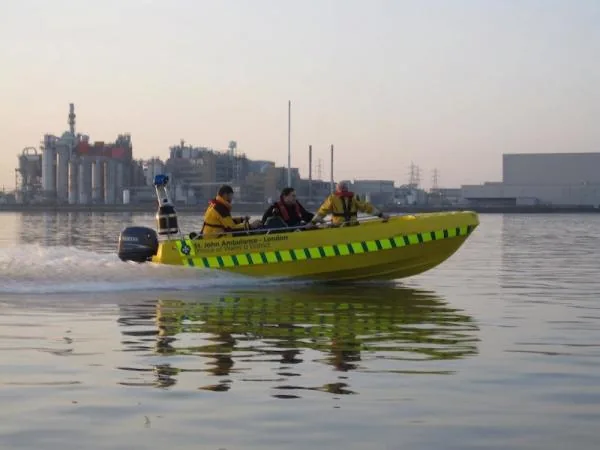 PIONER MULTI III viewed from the side while underway, with four people, an outboard motor and an industrial harbor in the background
