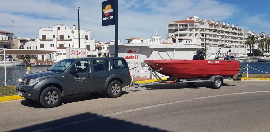 Pioner Multi 3, red, viewed from the side on a trailer next to a pickup truck, at a marina.