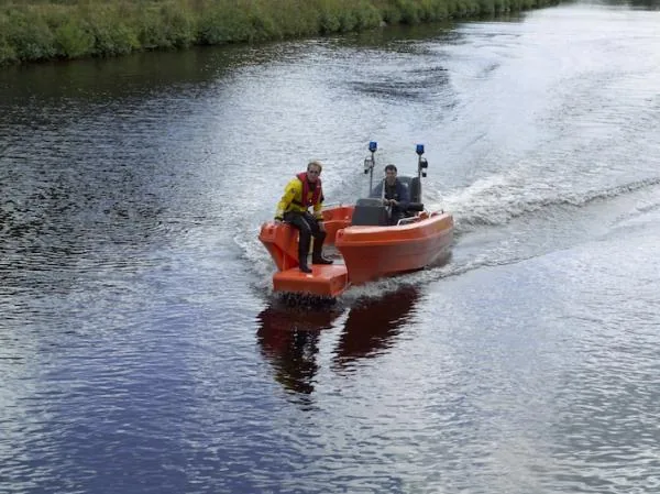 5df043325195edce89f6f19f7733b606 PIONER MULTI III sailing along a river, front exterior view with two people on board and a wake behind