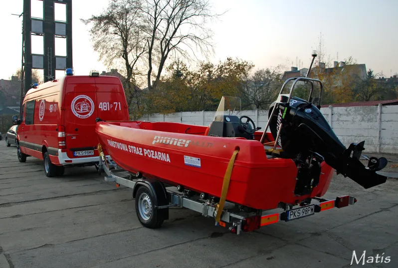 PIONER MULTI III, red boat viewed from the stern on a trailer, with an outboard motor and a red van in the background.