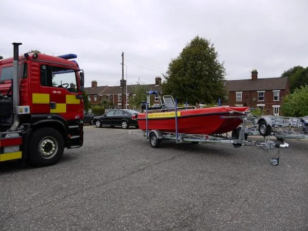 PIONER MULTI III, exterior side view on a trailer, next to a fire truck in a marina parking lot