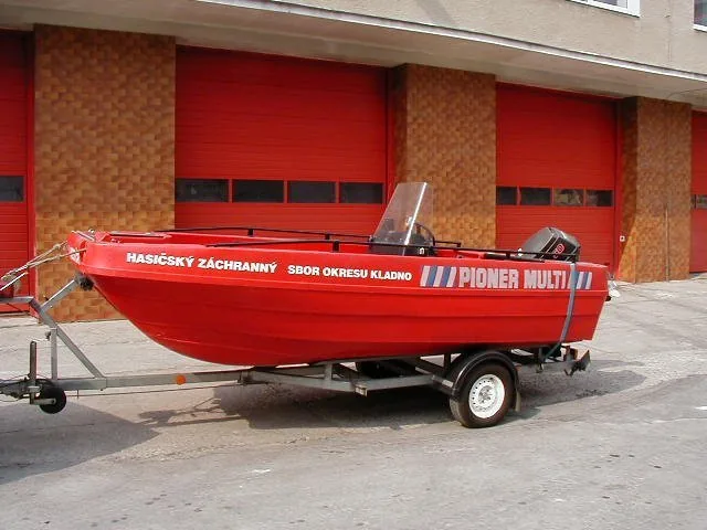 Exterior of a red PIONER MULTI III on a trailer, with windshield, console and outboard motor in front of a garage.