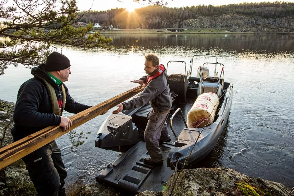 PIONER MULTI III seen from the side on a lake, with two men, boards, an outboard motor and cargo on board.
