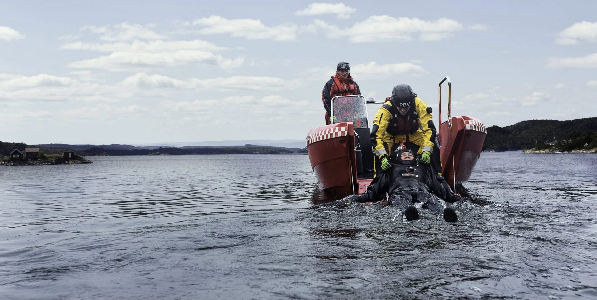 PIONER MULTI III viewed from the water, with two people and a diver at the stern.