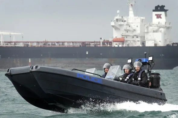 Pioner Multi III police boat cruising in profile, with three crew members and a cargo ship in the background