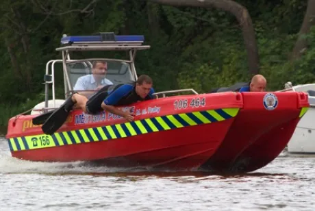 Red PIONER MULTI III viewed from the side, with three people aboard, a cabin, and yellow and green reflective stripes