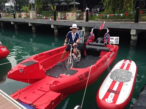 PionerMultiIII PIONER MULTI III red, viewed from above, with a person on a bicycle, a dock, and a paddleboard.