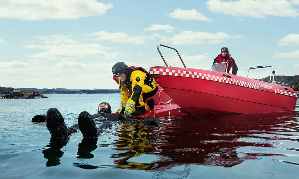 Exterior of the PIONER MULTI III on the water, with a diver next to the hull and a person aboard.