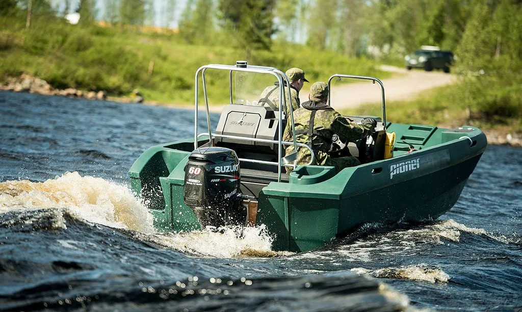 Exterior of the PIONER MULTI III navigating a river, seen from the stern and starboard side, with two people on board.