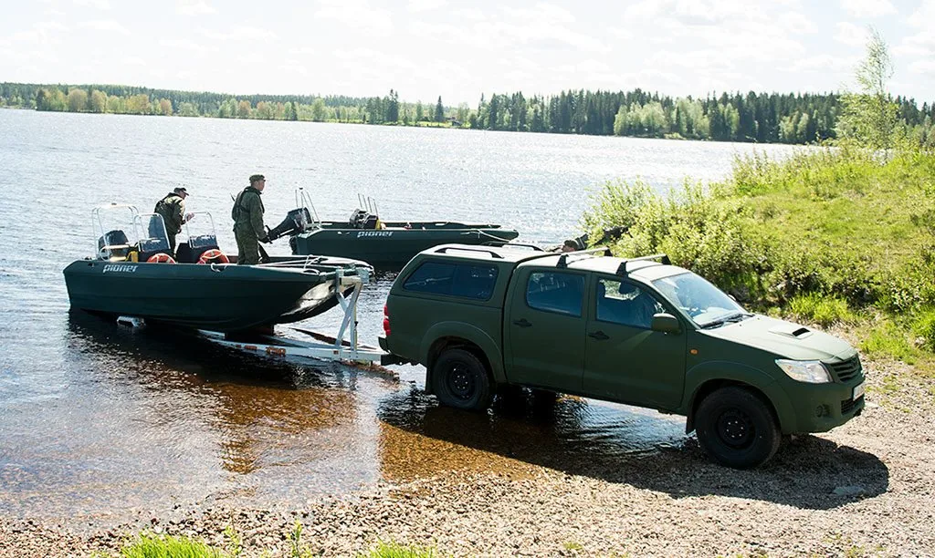 PIONER MULTI III on the shore of a lake, towed by a green vehicle, with two people beside the boat.