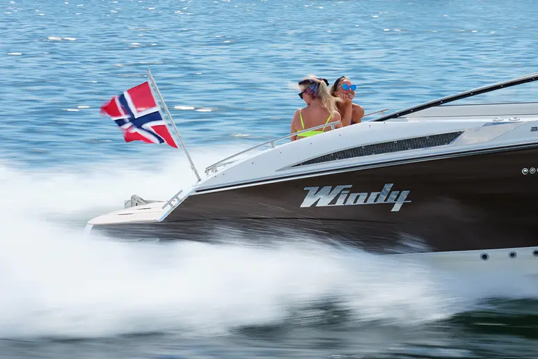 Windy 32 Grand Zonda cruising in profile, with two people on board, Norwegian flag and a wake.