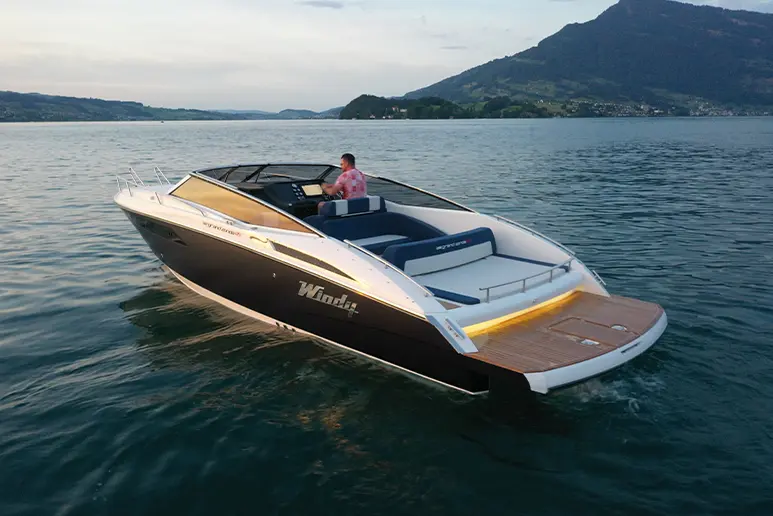 Windy 32 Grand Zonda viewed from the stern, cruising on a lake with mountains in the background.