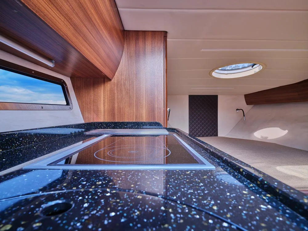 Windy 32 Grand Zonda: interior viewed from the galley, with a black countertop, wooden cabinets, a window and an overhead hatch
