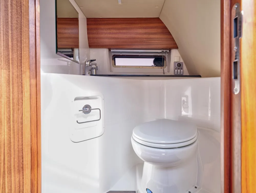 Interior of the bathroom of the Windy 32 Grand Zonda, with toilet, sink, window, and wood paneling.