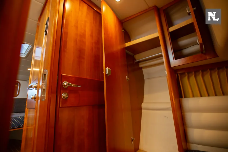 Interior del Windy 32 Scirocco: puerta de madera, armarios abiertos y litera tapizada en crema.